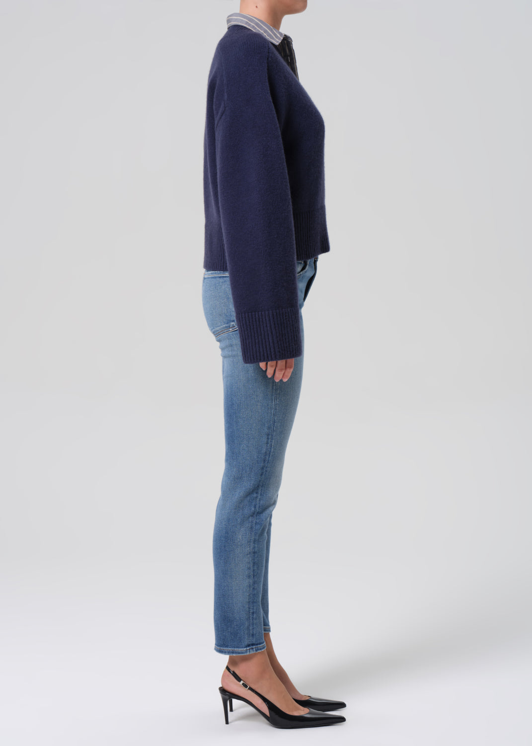 Person wearing a navy sweater and blue jeans on a white background