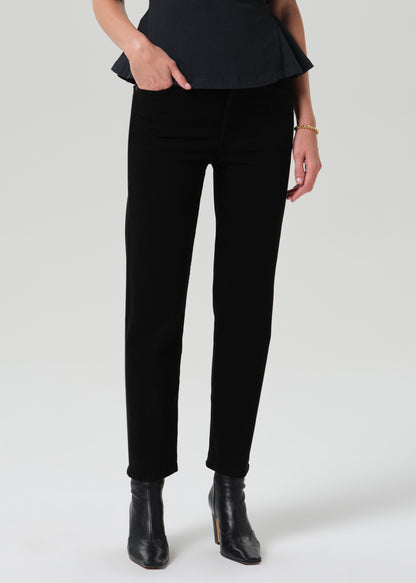 A model wearing black slim-fit ankle-length pants with a peplum top and black ankle boots, shown from the waist down against a grey background.
