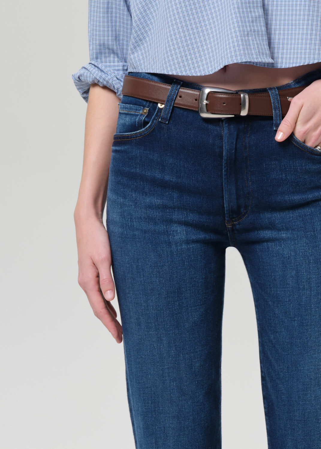Person wearing a light blue button-up shirt and dark blue jeans on a grey background