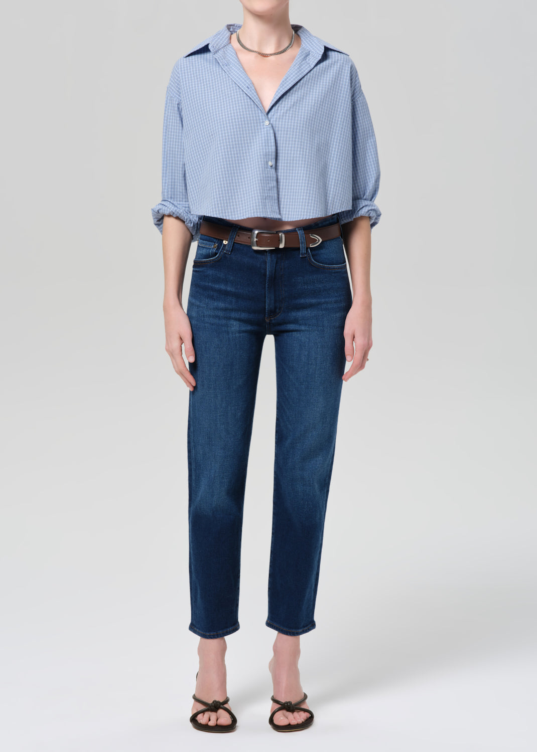 Person wearing a light blue button-up shirt and dark blue jeans on a grey background