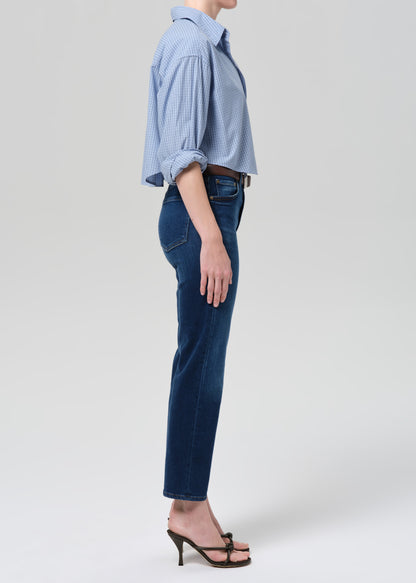 Person wearing a light blue button-up shirt and dark blue jeans on a grey background