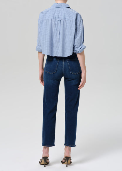 Person wearing a light blue button-up shirt and dark blue jeans on a grey background
