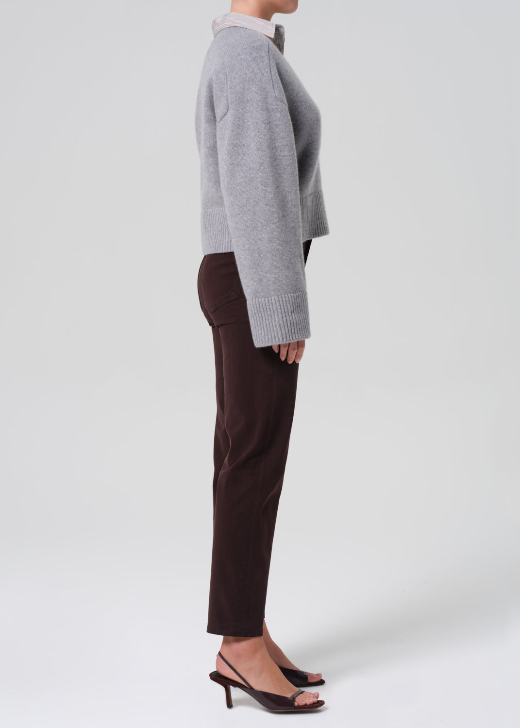 Person wearing a gray sweater and brown pants on a white background