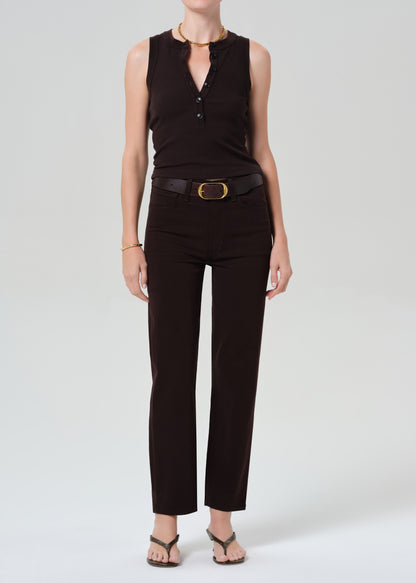 Person wearing a brown sleeveless top and brown pants with a belt on a grey background