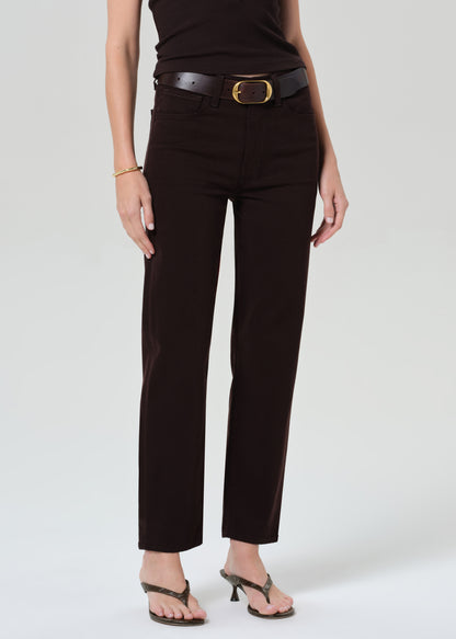 Person wearing a brown sleeveless top and brown pants with a belt on a grey background