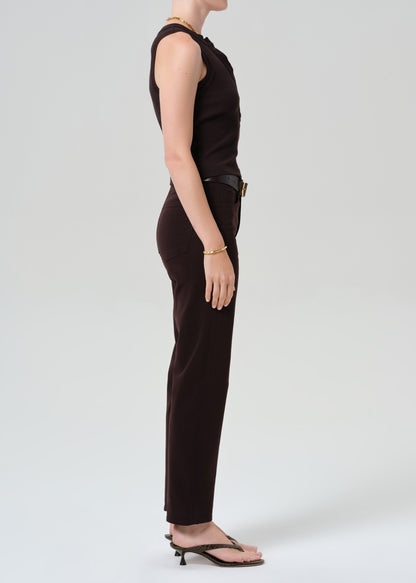 Person wearing a brown sleeveless top and brown pants with a belt on a grey background