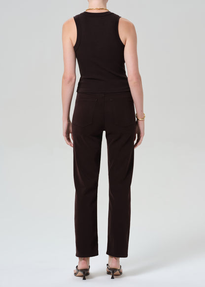 Person wearing a brown sleeveless top and brown pants with a belt on a grey background