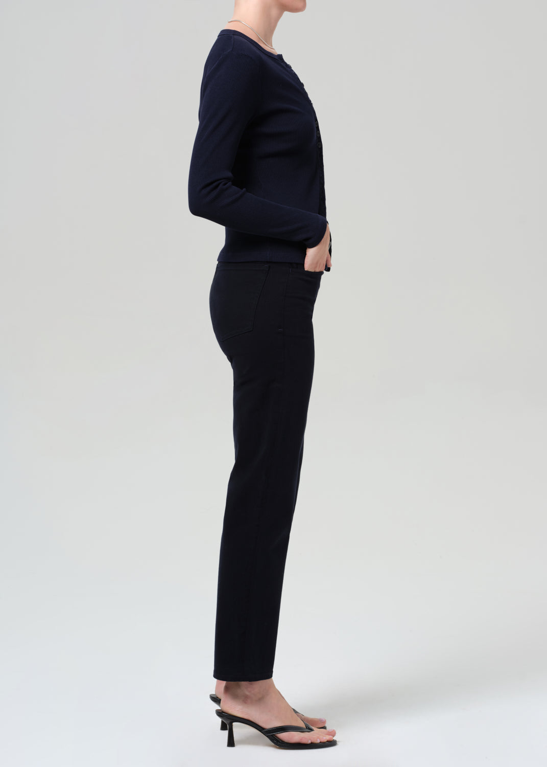 Person wearing a navy navy cardigan and navy pants on a grey background