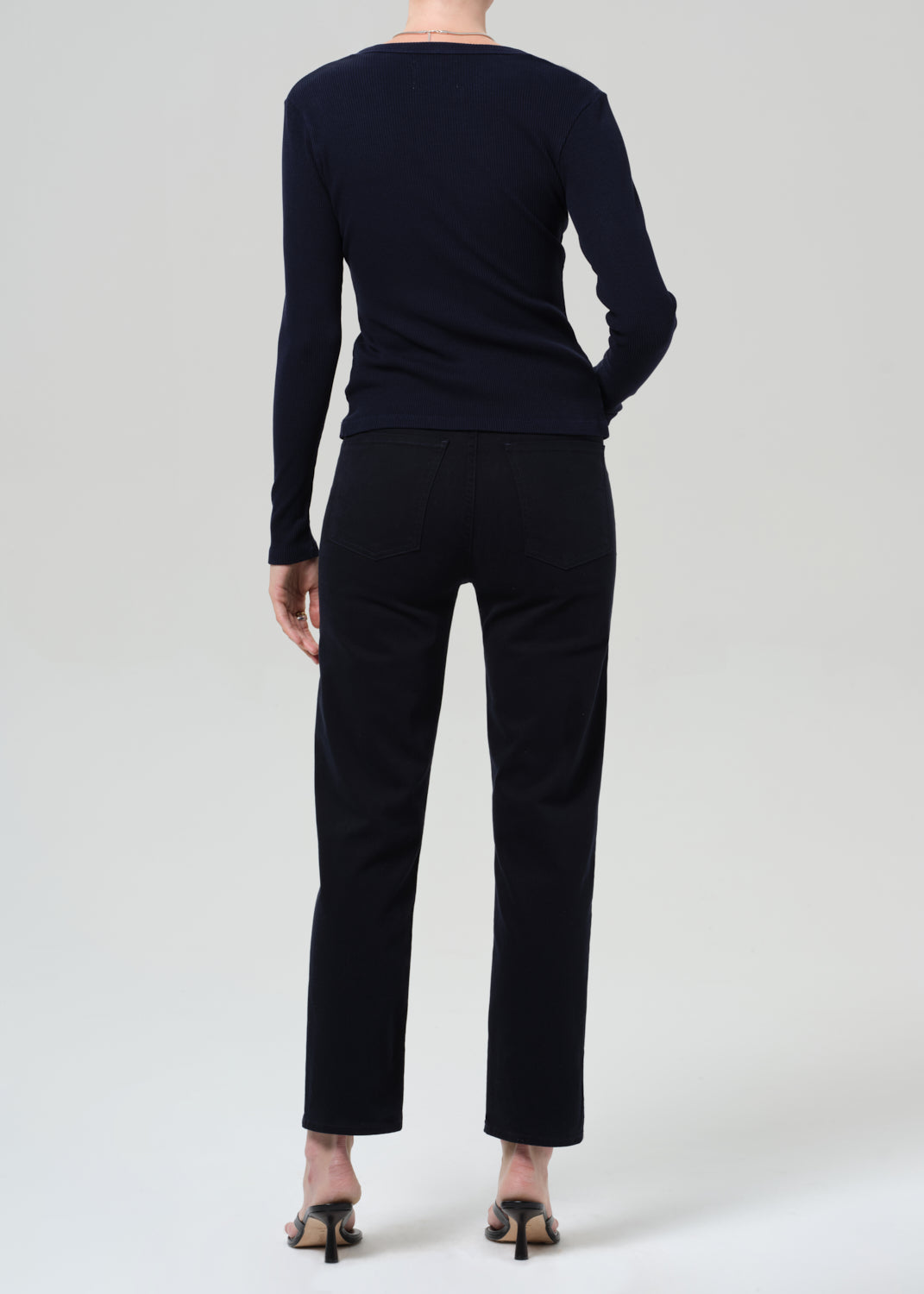 Person wearing a navy navy cardigan and navy pants on a grey background