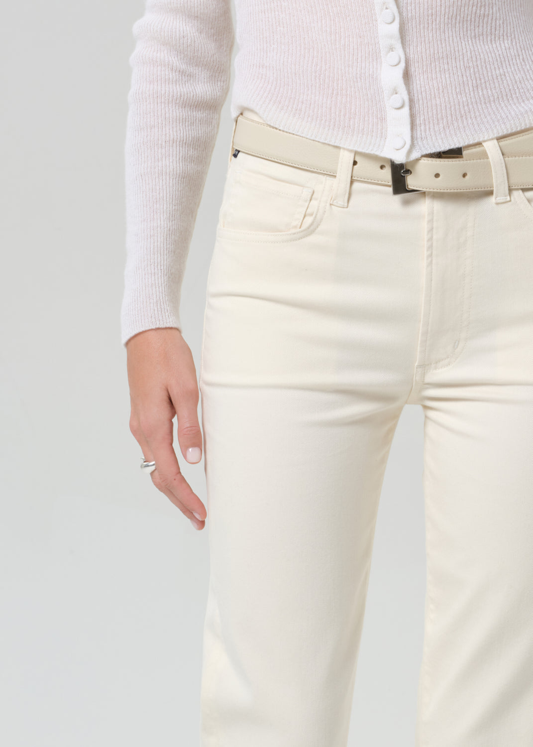 Person wearing white jeans with a beige belt on a light gray background