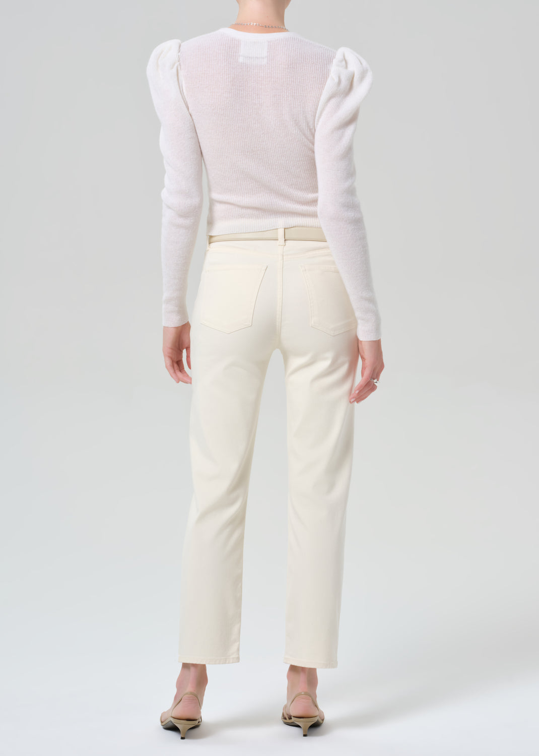 Person wearing a white long-sleeve top and cream-colored pants on a plain background