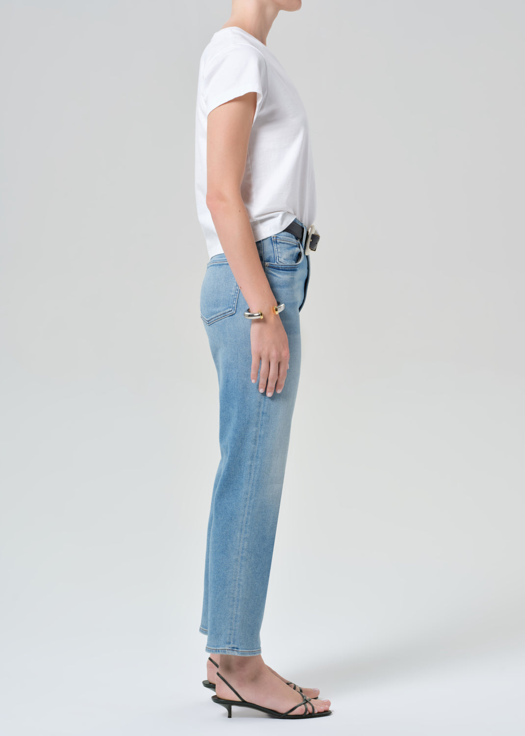Person wearing a white t-shirt and light blue jeans on a plain background