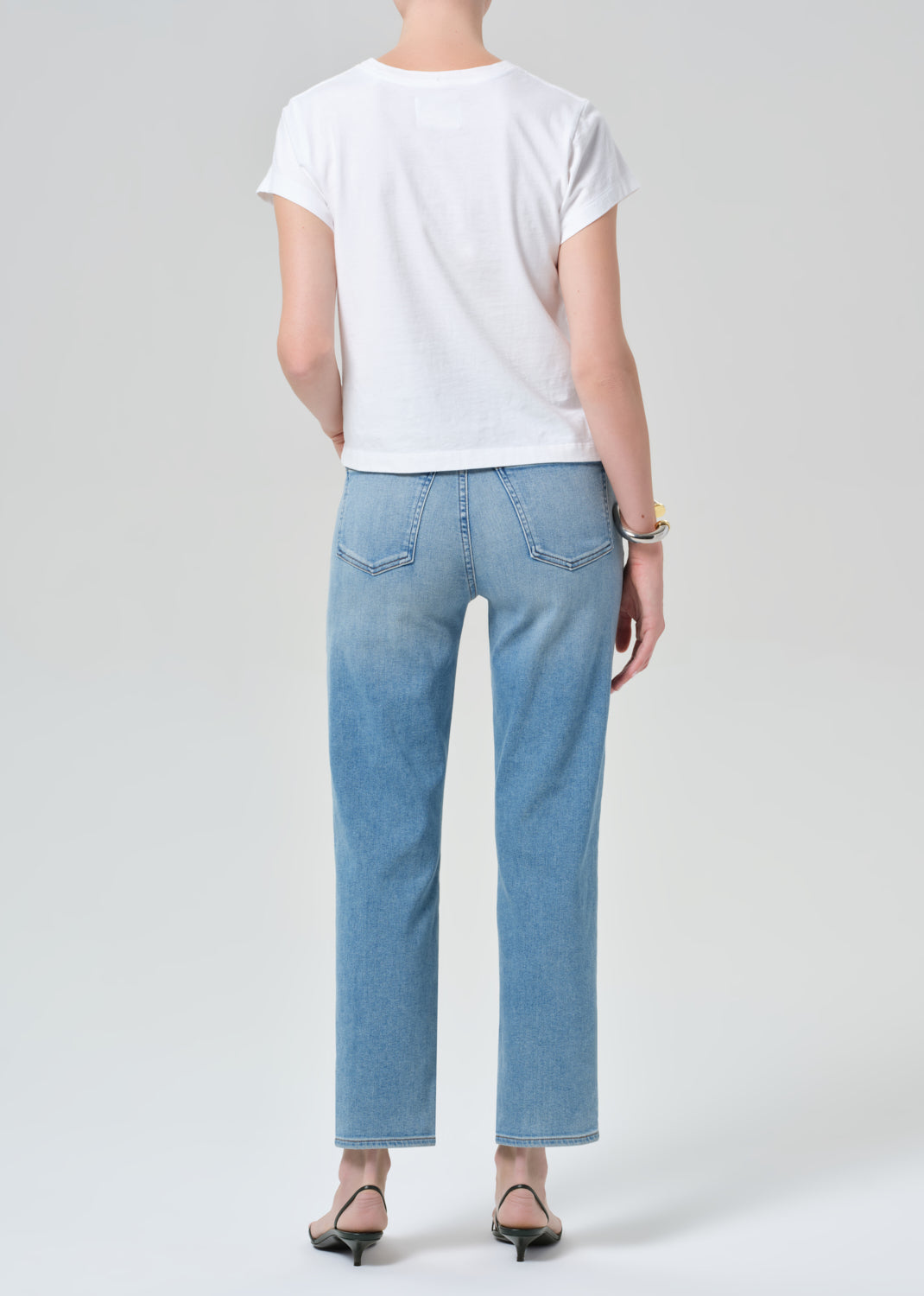 Person wearing a white t-shirt and light blue jeans on a plain background