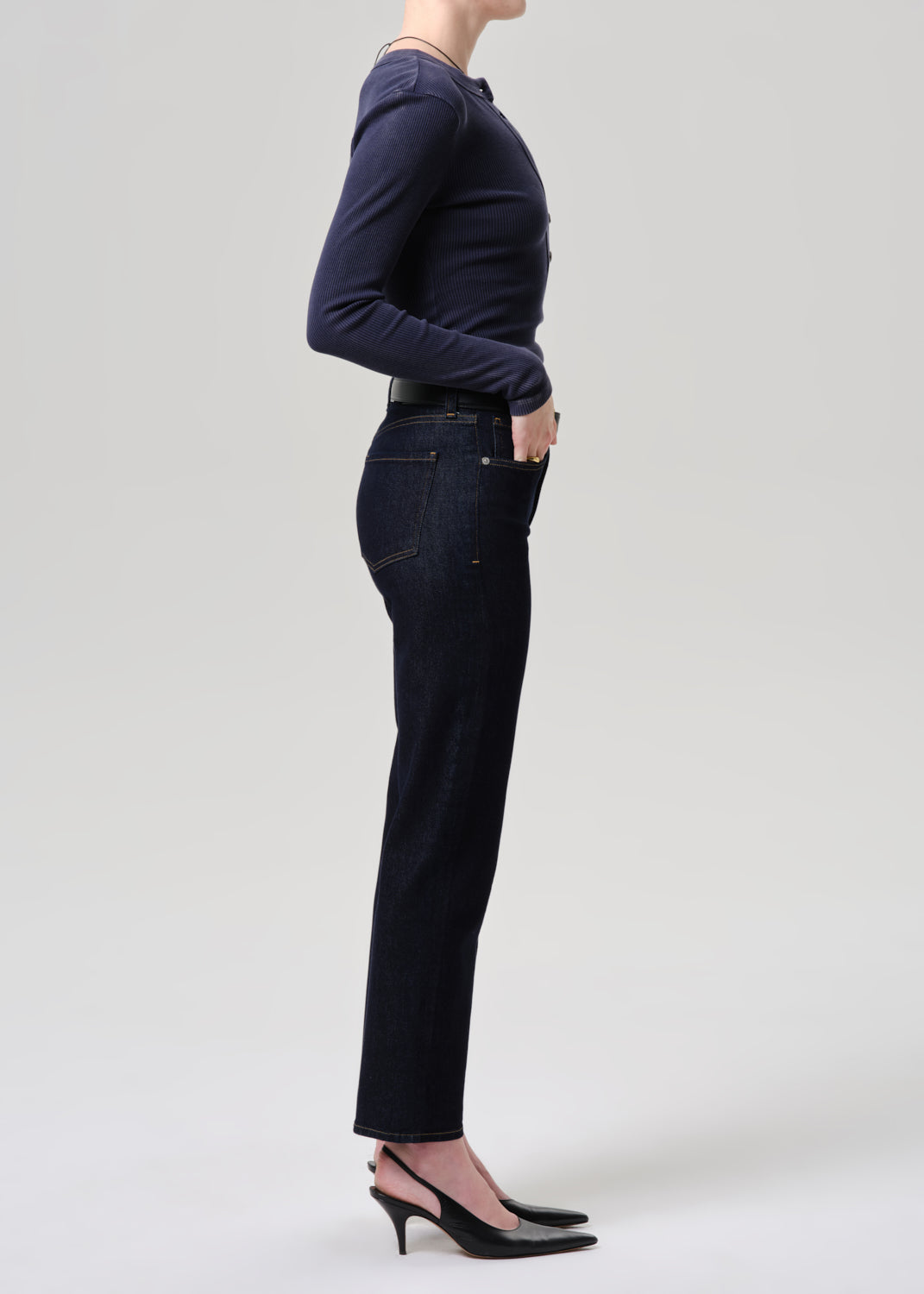 Person wearing a navy long-sleeve top and dark jeans on a grey background