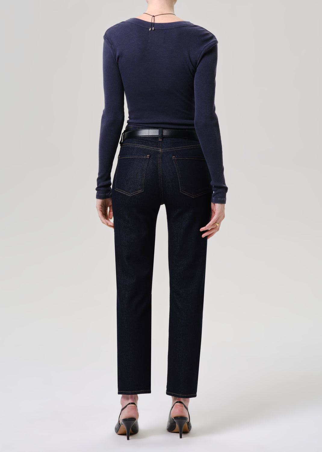 Person wearing a navy long-sleeve top and dark jeans on a grey background