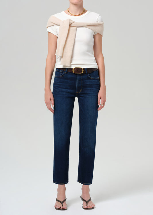 Person wearing a white top, beige sweater, and blue jeans on a plain background