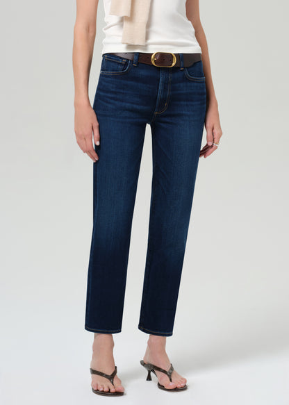 Person wearing a white top, beige sweater, and blue jeans on a plain background