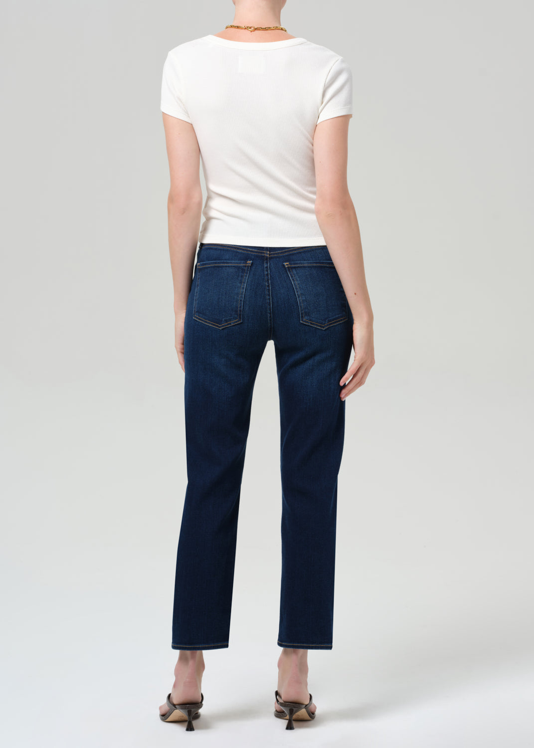 Person wearing a white top, beige sweater, and blue jeans on a plain background