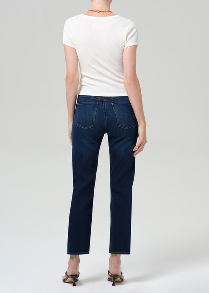 Person wearing a white top, beige sweater, and blue jeans on a plain background