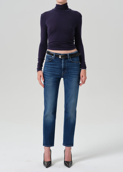 A model wearing a dark navy long-sleeve turtleneck top, blue cropped jeans with a black belt, and black pointed-toe heels, photographed against a grey background.