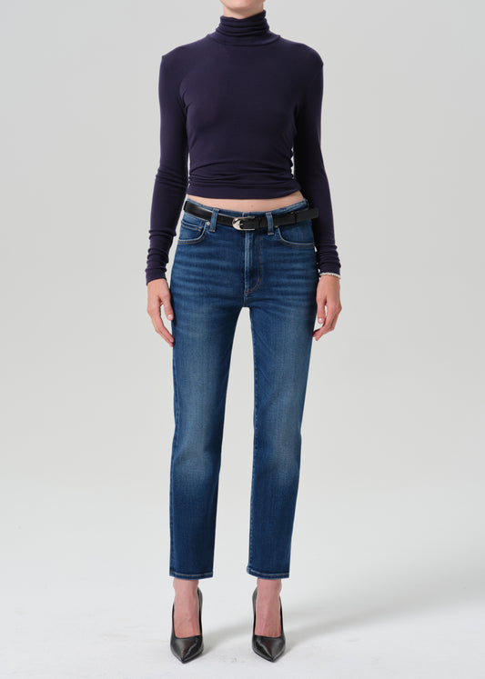 A model wearing a dark navy long-sleeve turtleneck top, blue cropped jeans with a black belt, and black pointed-toe heels, photographed against a grey background.