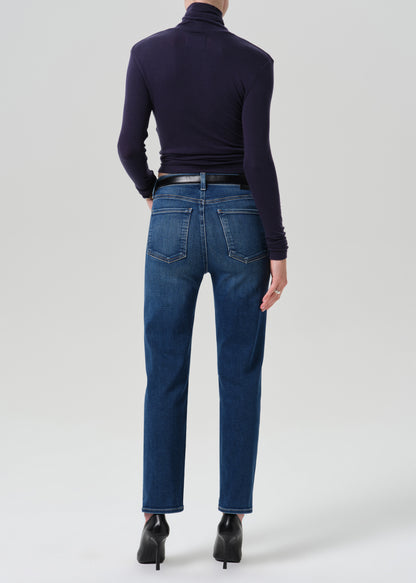 A model shown from the back wearing dark blue straight-leg jeans, a dark navy turtleneck top, a black belt, and black high-heeled boots against a grey background.