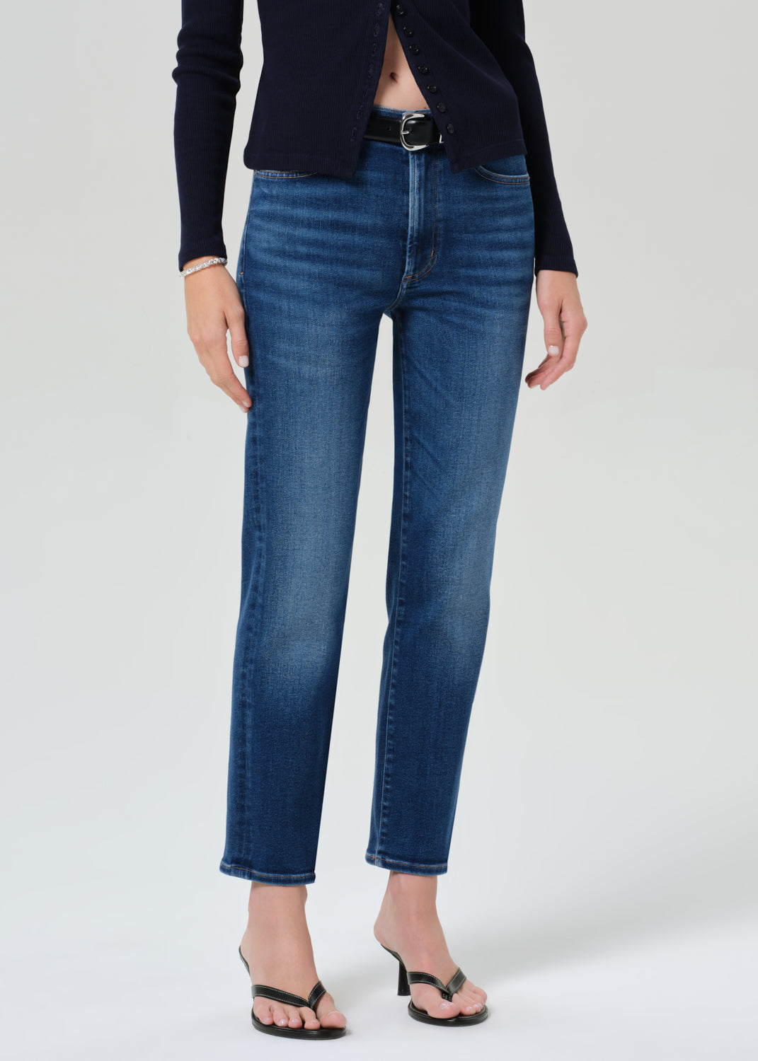 Person wearing a navy cardigan and blue jeans on a grey background