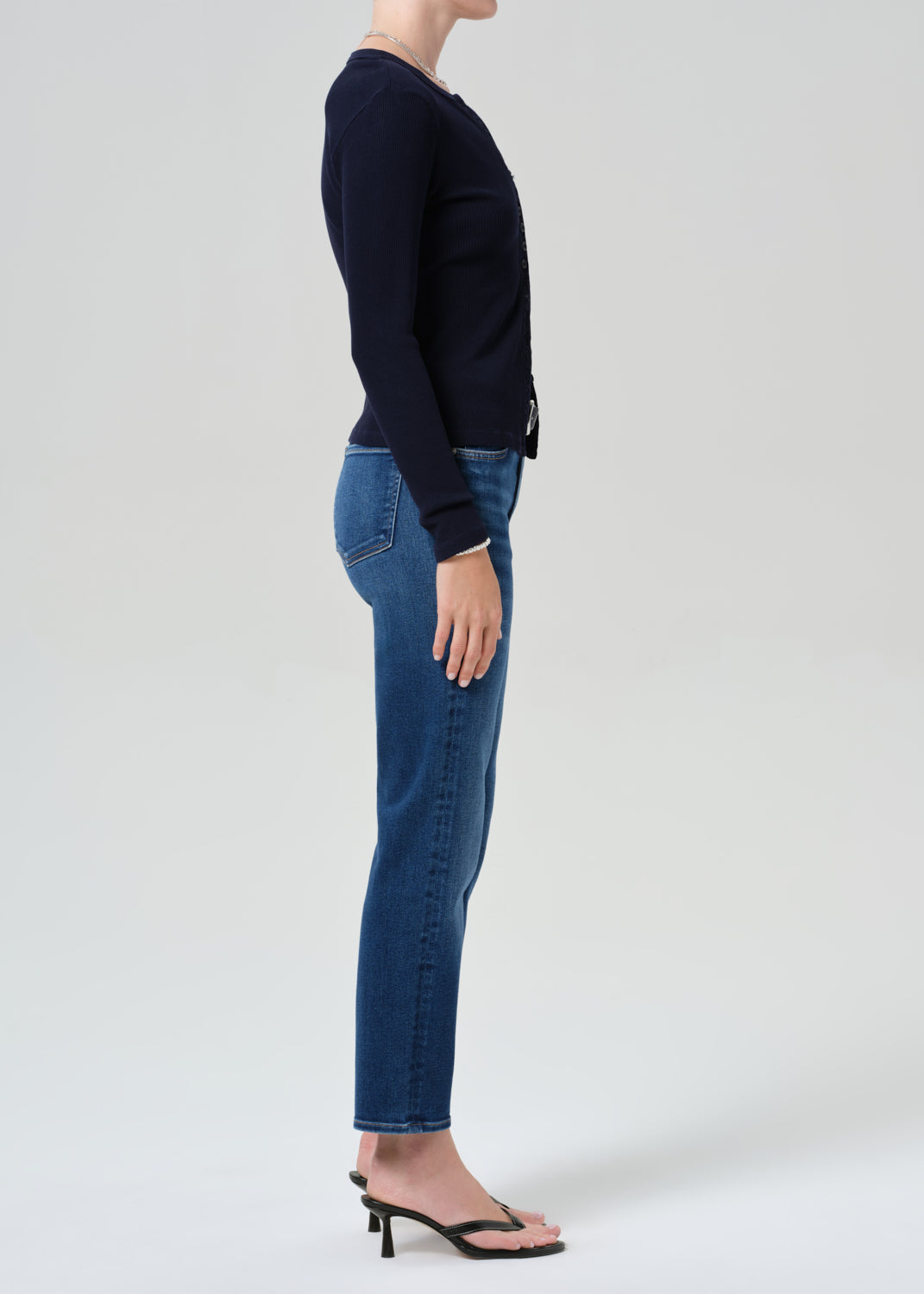 Person wearing a navy cardigan and blue jeans on a grey background