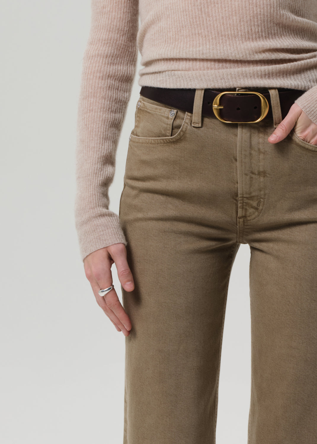 Person wearing beige sweater and brown pants with a black belt on a light gray background