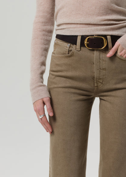 Person wearing beige sweater and brown pants with a black belt on a light gray background