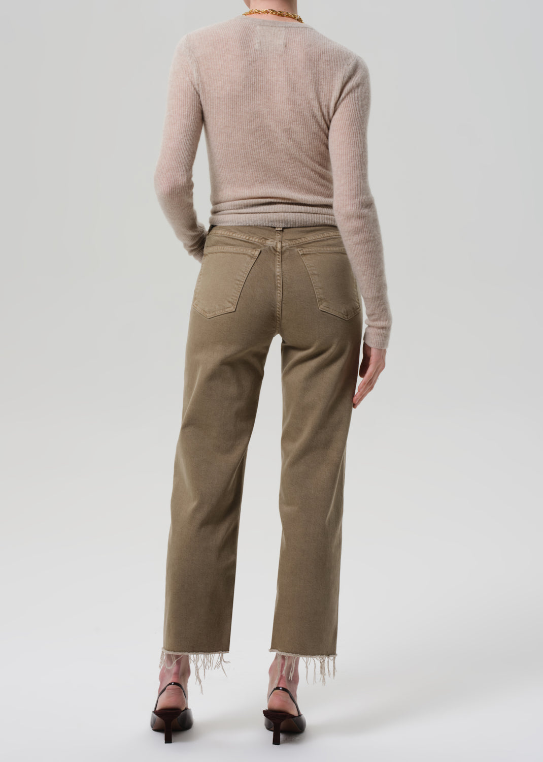 Person wearing a beige sweater and khaki pants on a white background