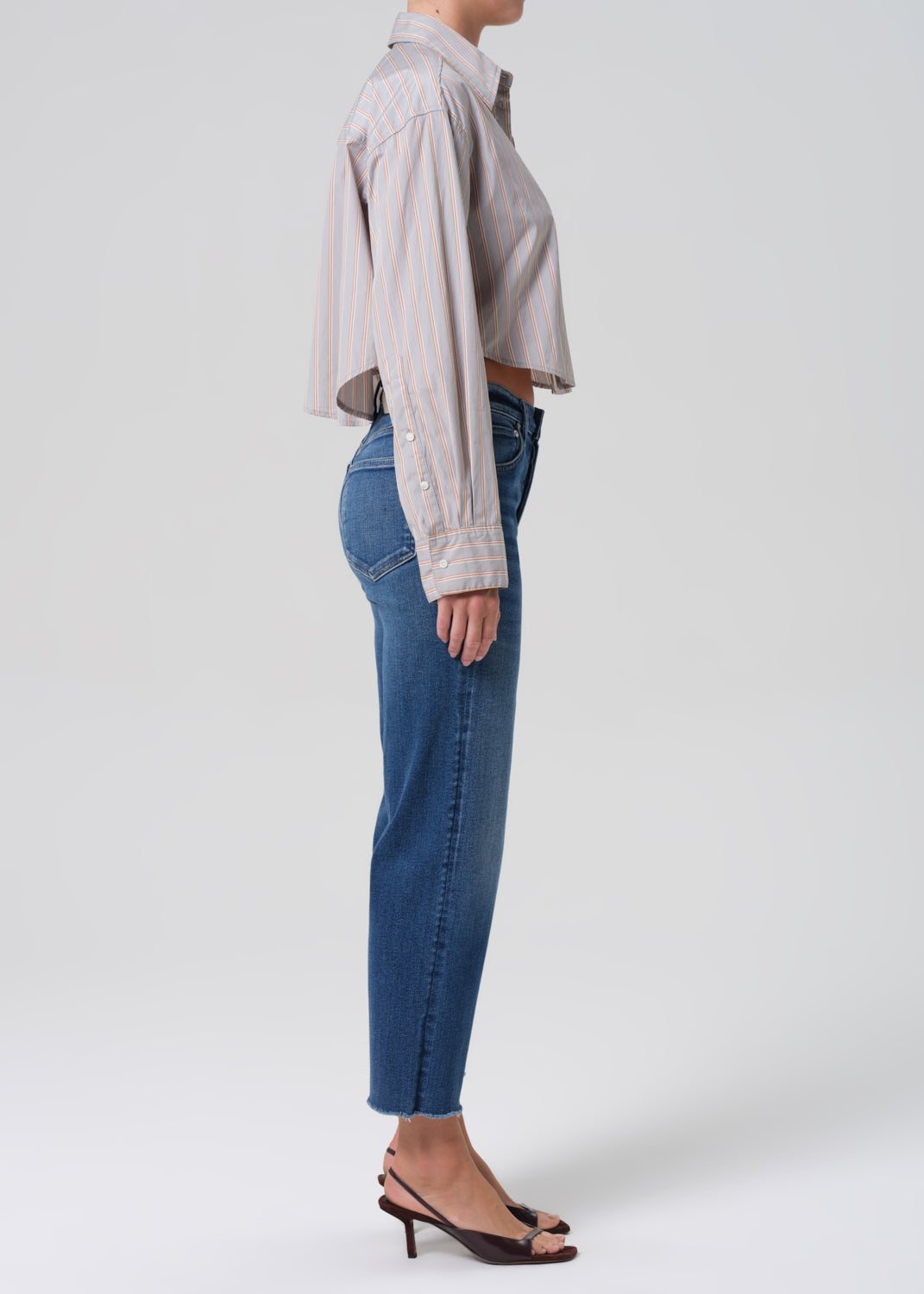 Person wearing a light gray stripe shirt and blue jeans on a grey background