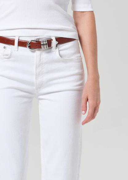 Person wearing a white shirt and white pants with a brown belt on a plain background