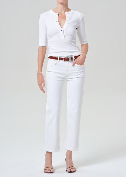 Person wearing a white shirt and white pants with a brown belt on a plain background