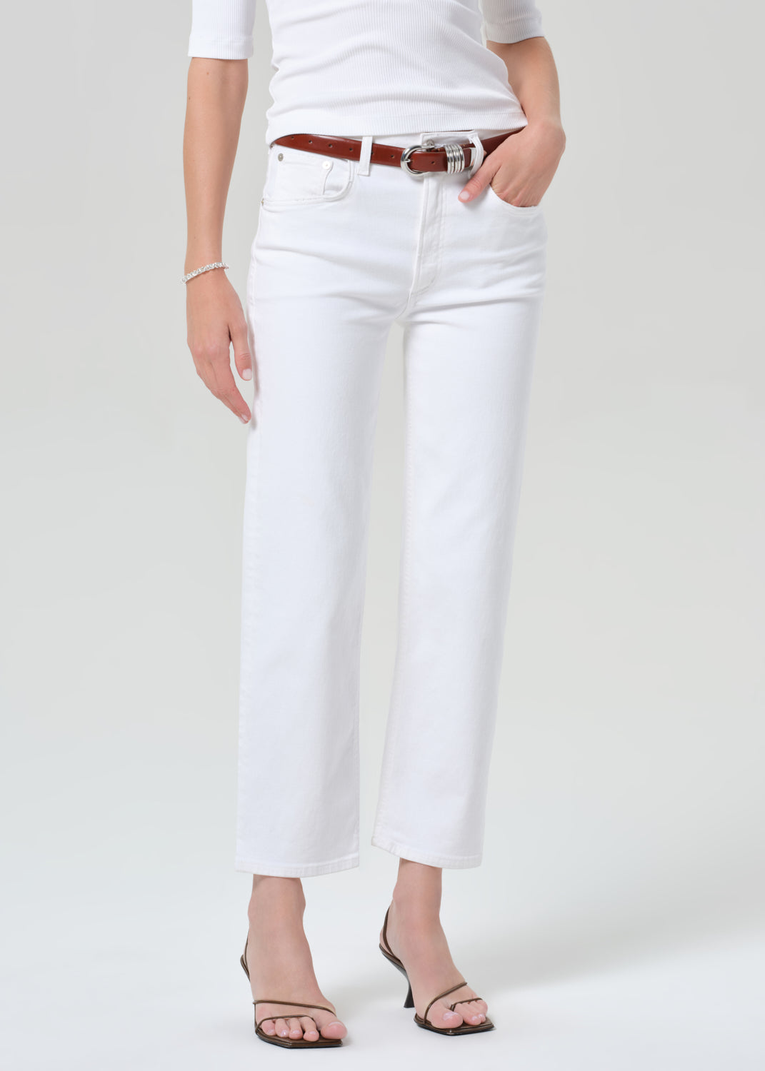 Person wearing a white shirt and white pants with a brown belt on a plain background