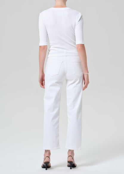 Person wearing a white shirt and white pants with a brown belt on a plain background