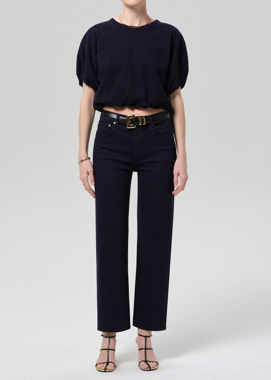 Person wearing a navy outfit with a belt on a grey background