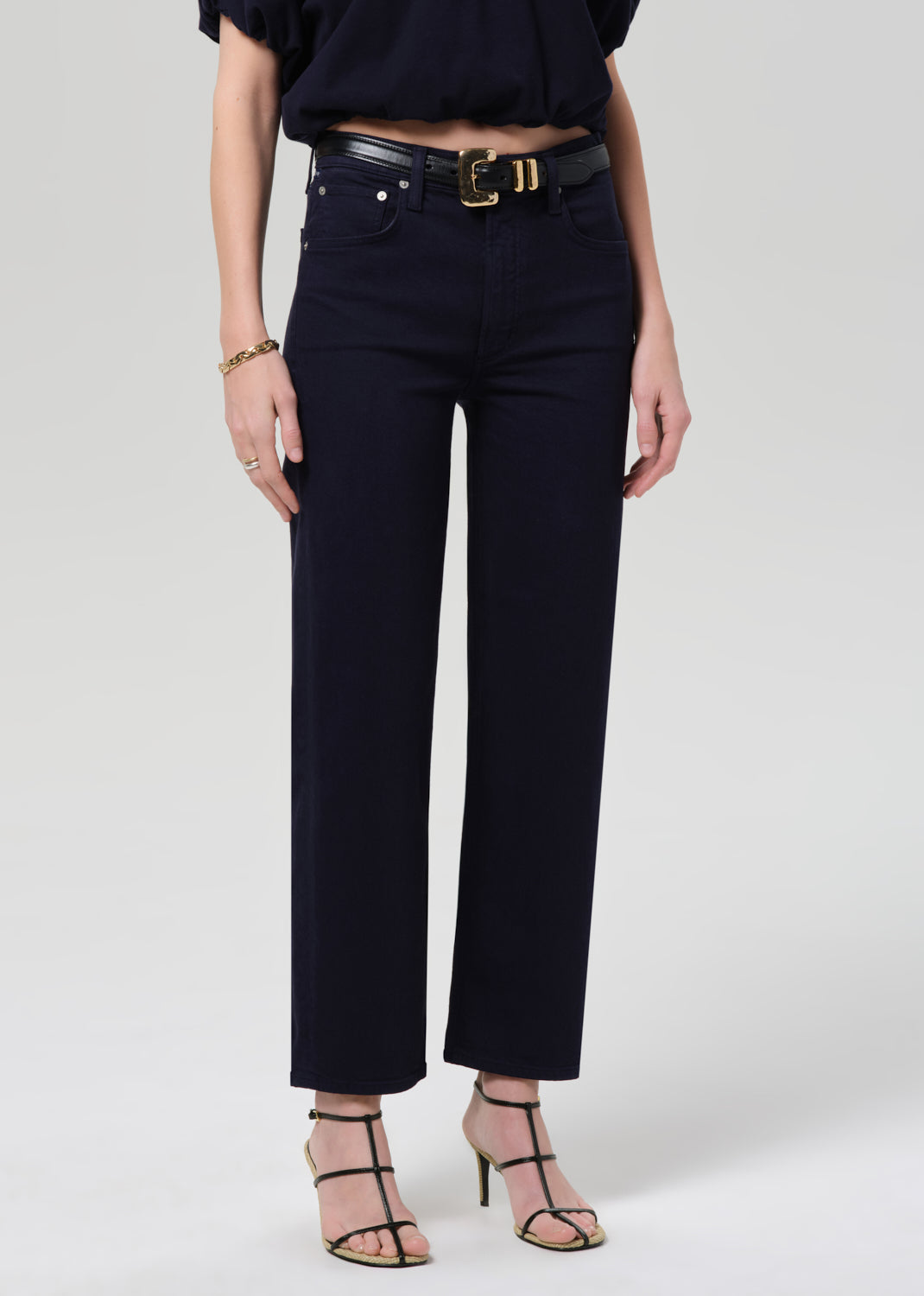 Person wearing black high-waisted jeans with a gold belt on a grey background
