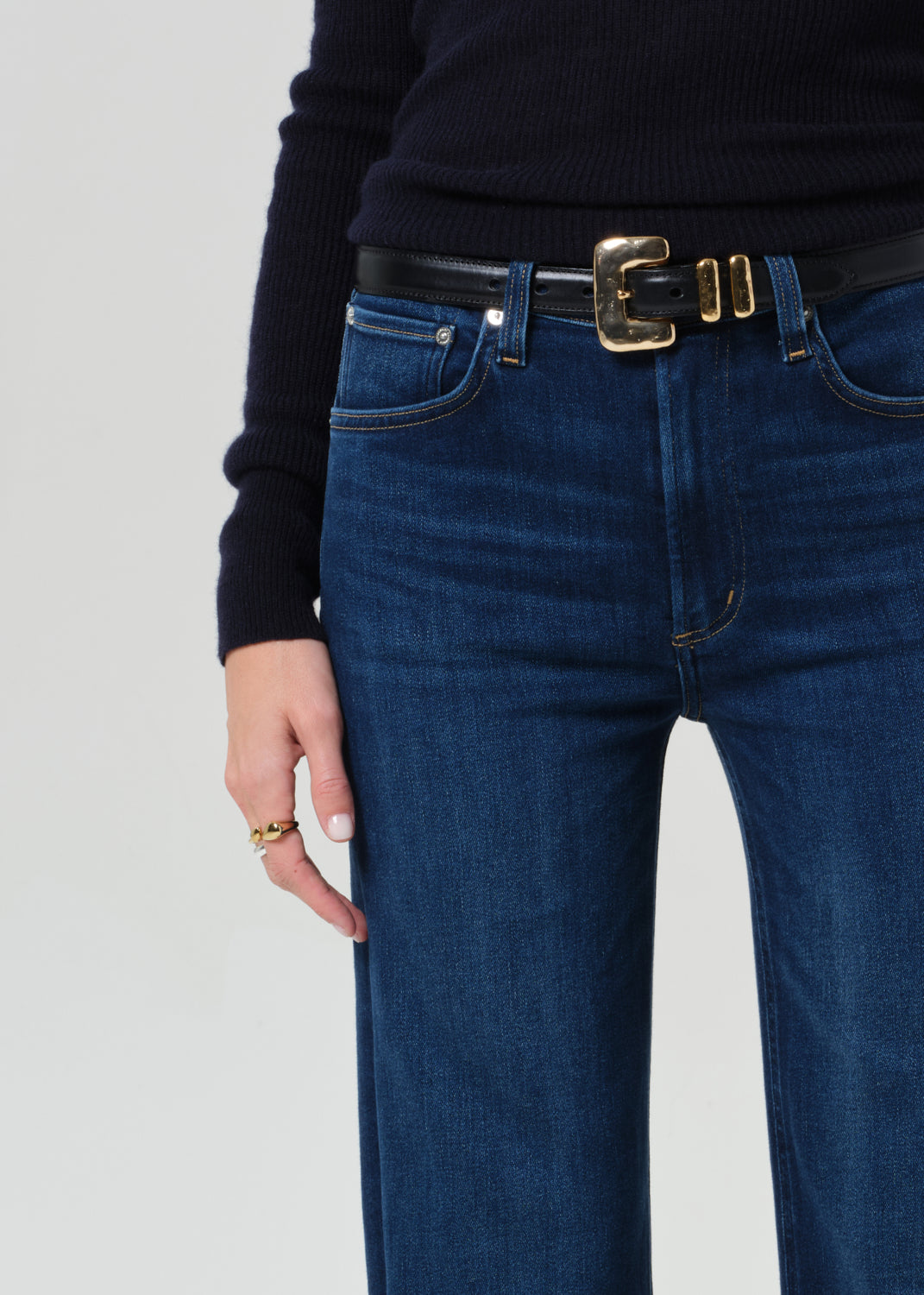 Person wearing blue jeans with a black belt on a light gray background