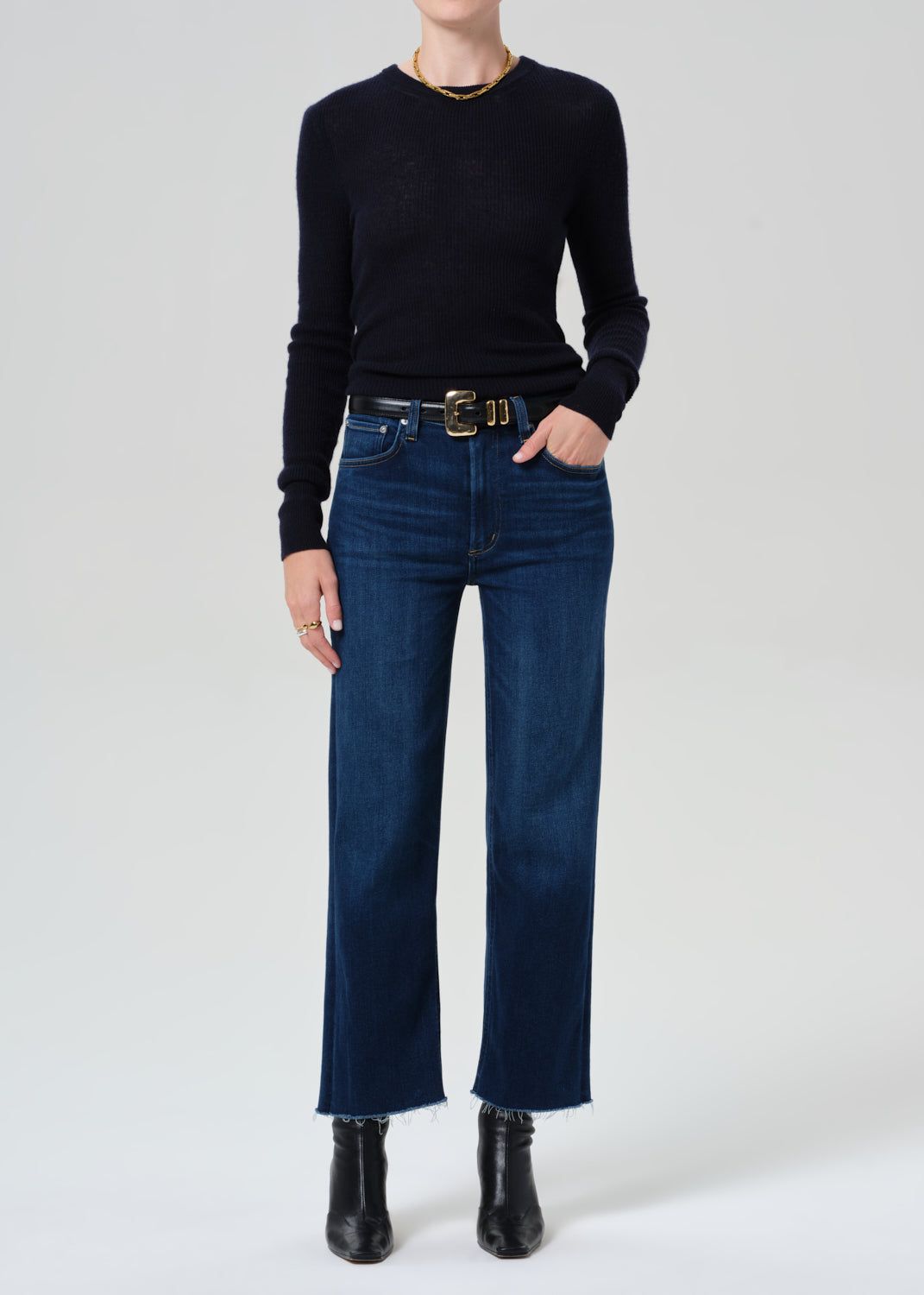 Person wearing a black sweater, blue jeans, and black boots on a white background