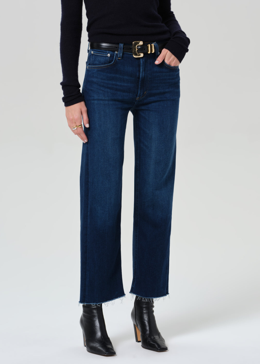 Person wearing blue jeans and black boots on a grey background