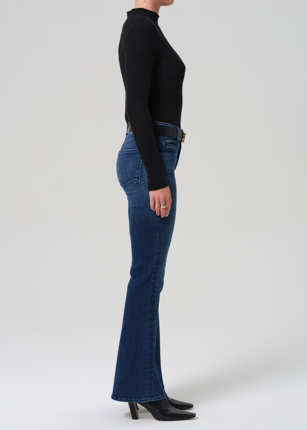 Person wearing blue flared jeans and a black top on a white background