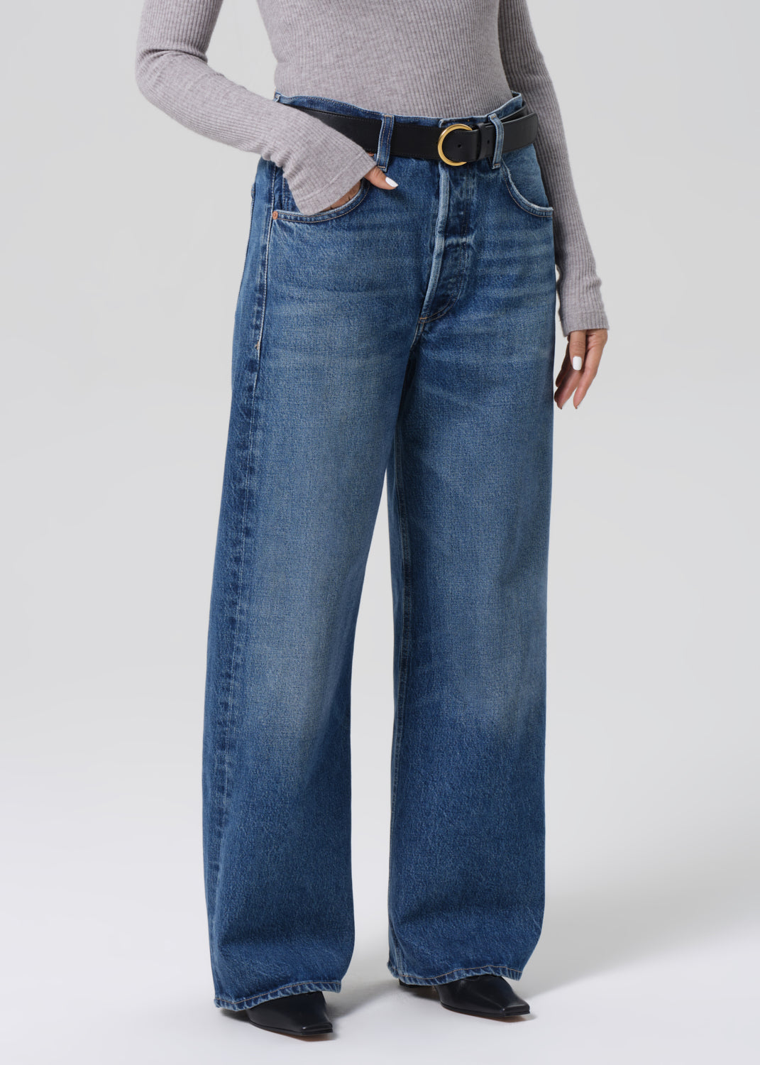 Person wearing blue jeans and a gray sweater on a grey background