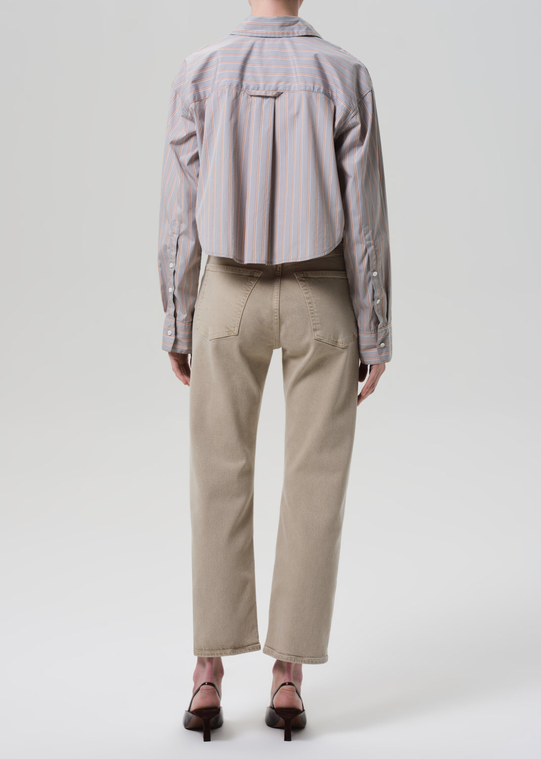 Person wearing a light gray shirt and beige pants on a white background