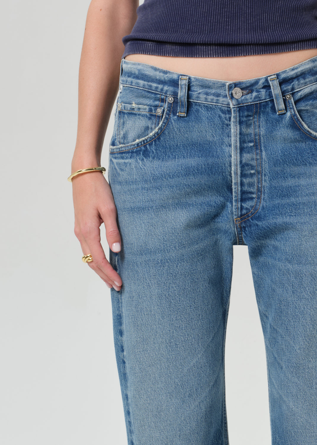 Person wearing a navy blue tee and light blue jeans on a grey background