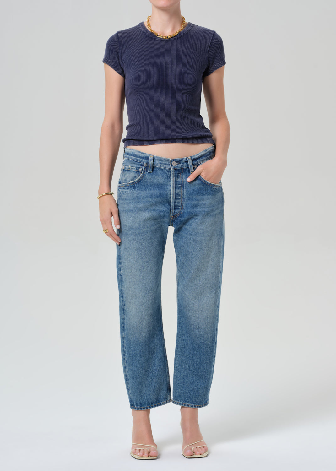 Person wearing a navy blue tee and light blue jeans on a grey background