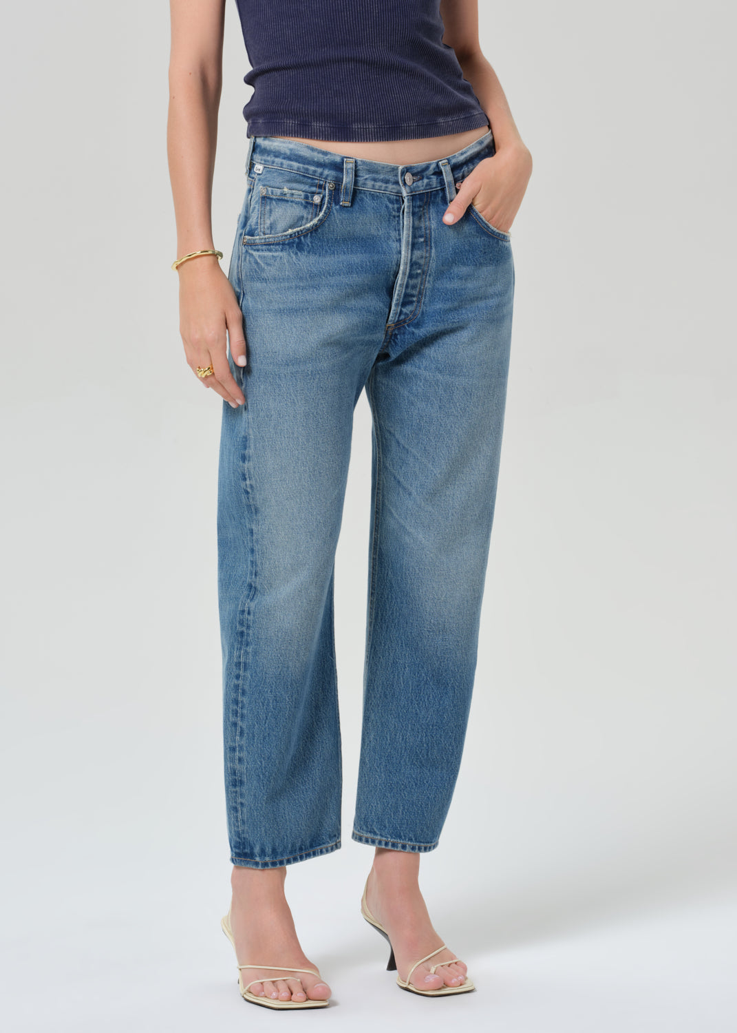 Person wearing a navy blue tee and light blue jeans on a grey background