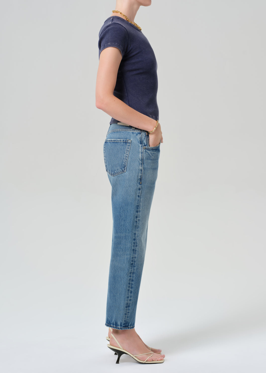 Person wearing a navy blue tee and light blue jeans on a grey background