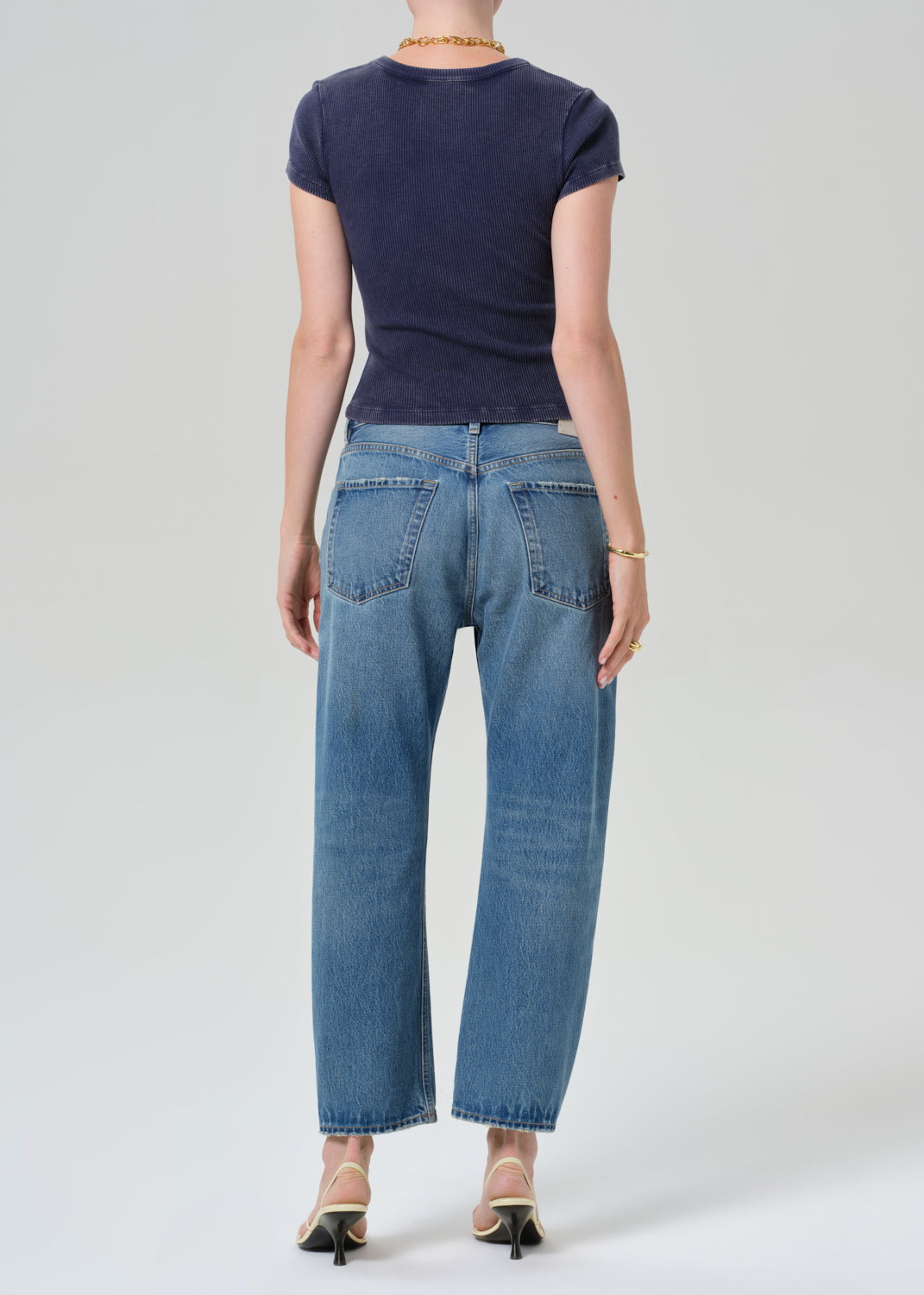 Person wearing a navy blue tee and light blue jeans on a grey background