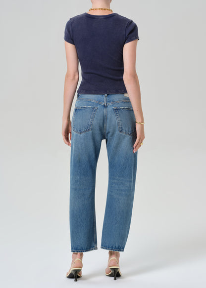 Person wearing a navy blue tee and light blue jeans on a grey background